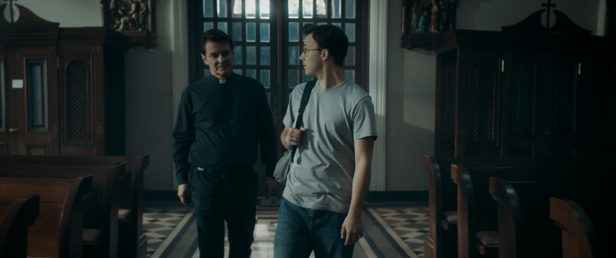 Ksiądz rozmawiający z młodym mężczyzną we wnętrzu kościoła w filmie Powołany 2